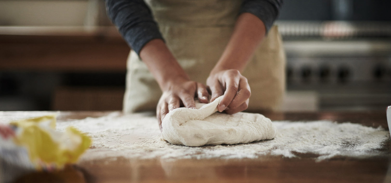 Person knetet Pizzateig auf Tisch
