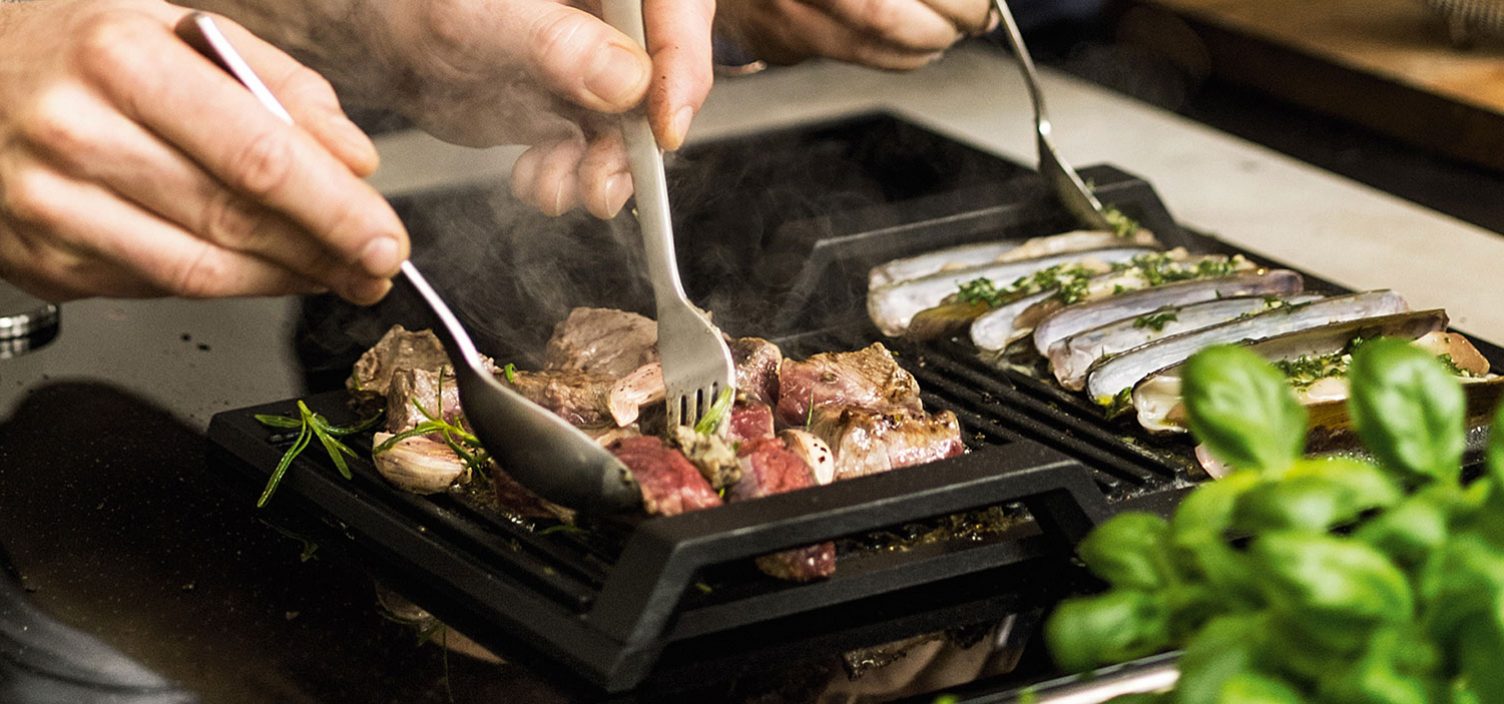 Nahaufnahme von Fleisch und Fisch auf Grillplatte auf einem Induktionskochfeld.